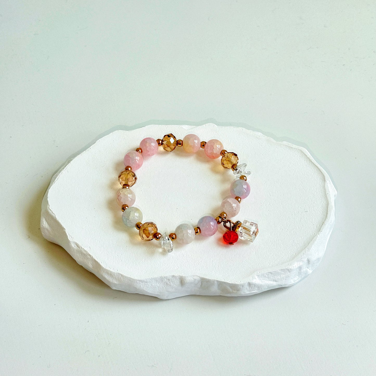 A simple, cute bracelet with pastel beads of pink, light blue, and light purple color, with bronze colored accents and a minimalist glass present charm.