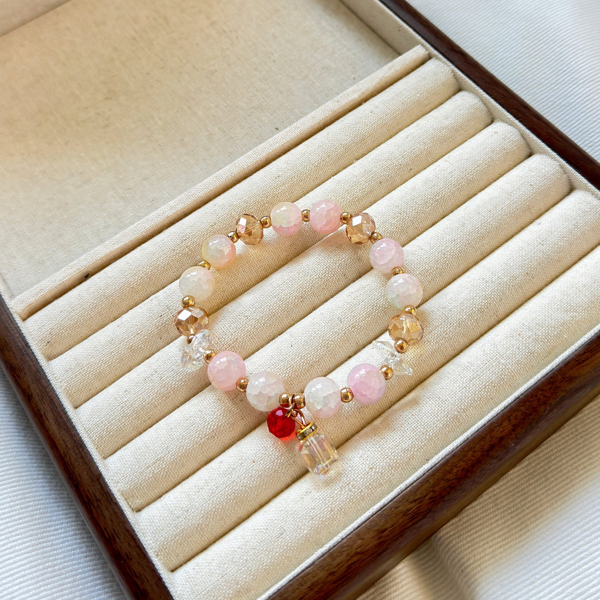 A high end jewelry piece, a cute bracelet with light colors and bronze accents, sitting in a warm wooden jewelry box.