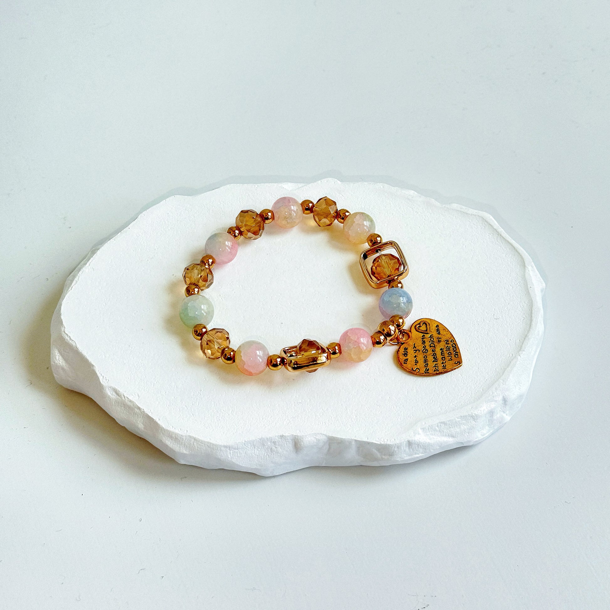 A simple, cute bracelet with pastel and bronze colored glass beads, along with bronze accents and a bronze hear charm, etched with different ways to say I love you in various languages.