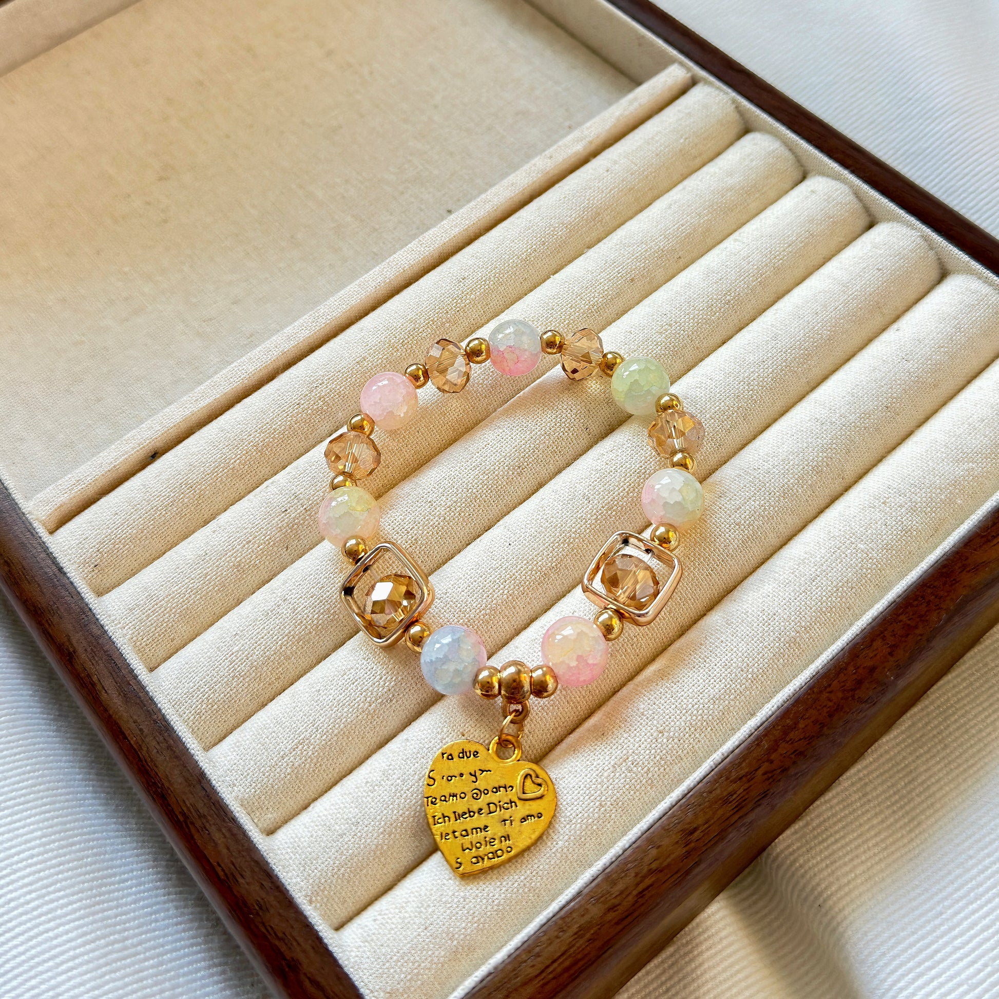 A glass beaded bracelet with bronze accents in a warm jewelry tray, with a charm that reads "I love you" in different languages, perfect for a gift for a woman in your life.