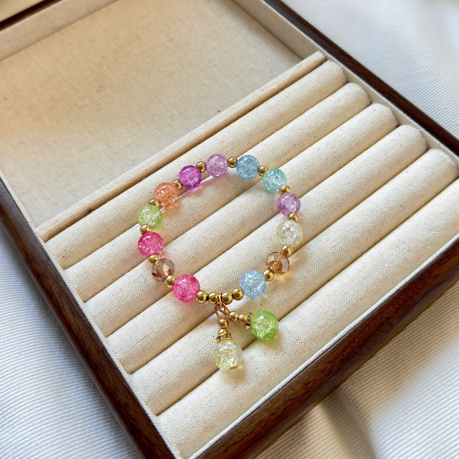 A bracelet with light pink glass beads, including pink, lavender, light orange, light blue, and a light grassy green, sitting in a warm jewelry tray.