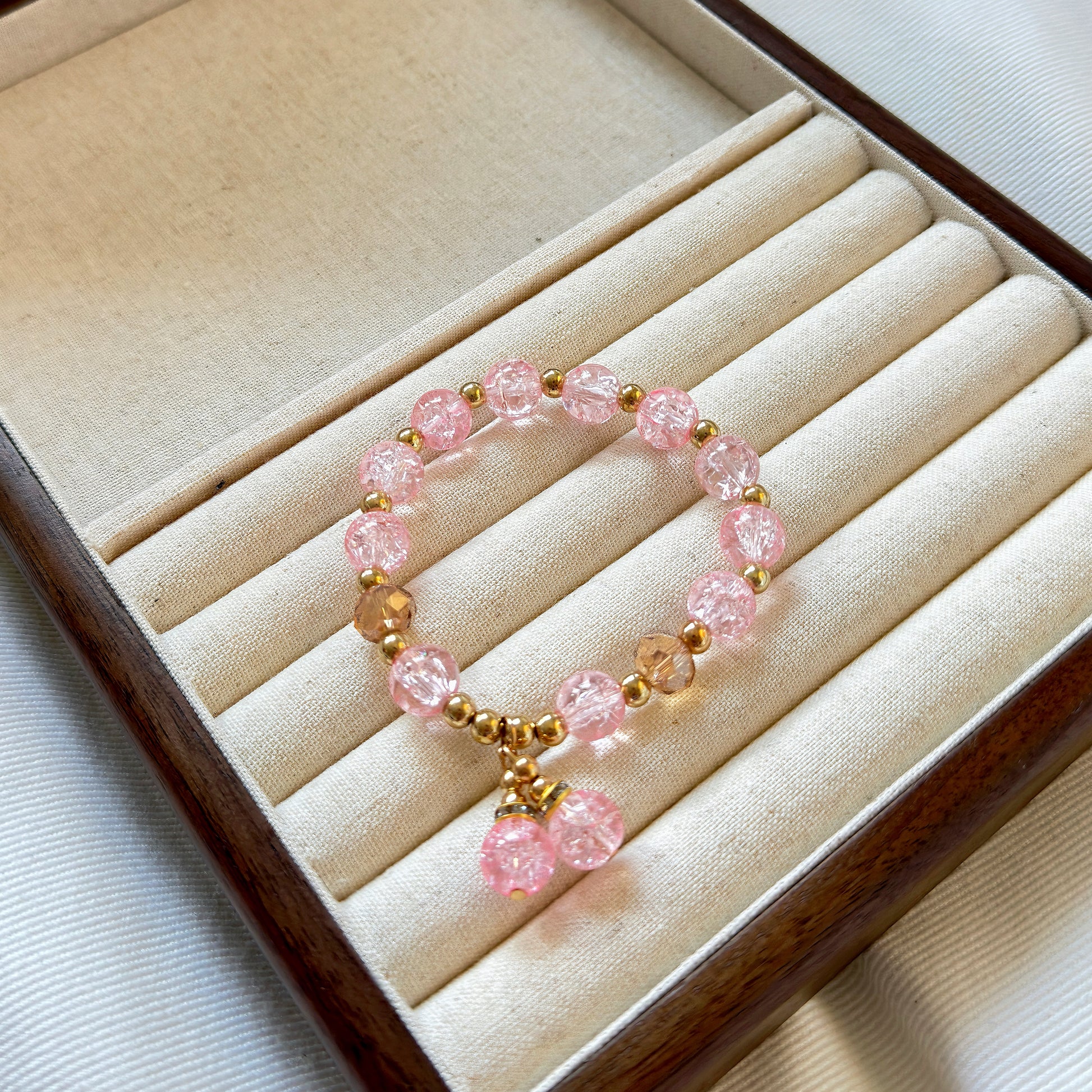 A cute pink bracelet with bronze colored accents sitting in a warm wooden jewelry box.