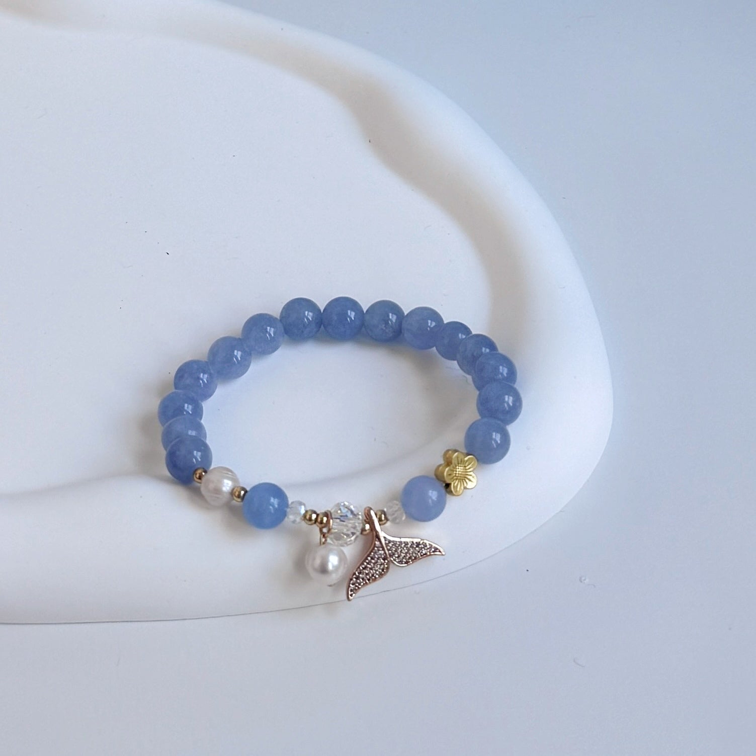 Aquamarine beaded bracelet with pearls and a gold charm in the shape of a mermaid or dolphin tail.