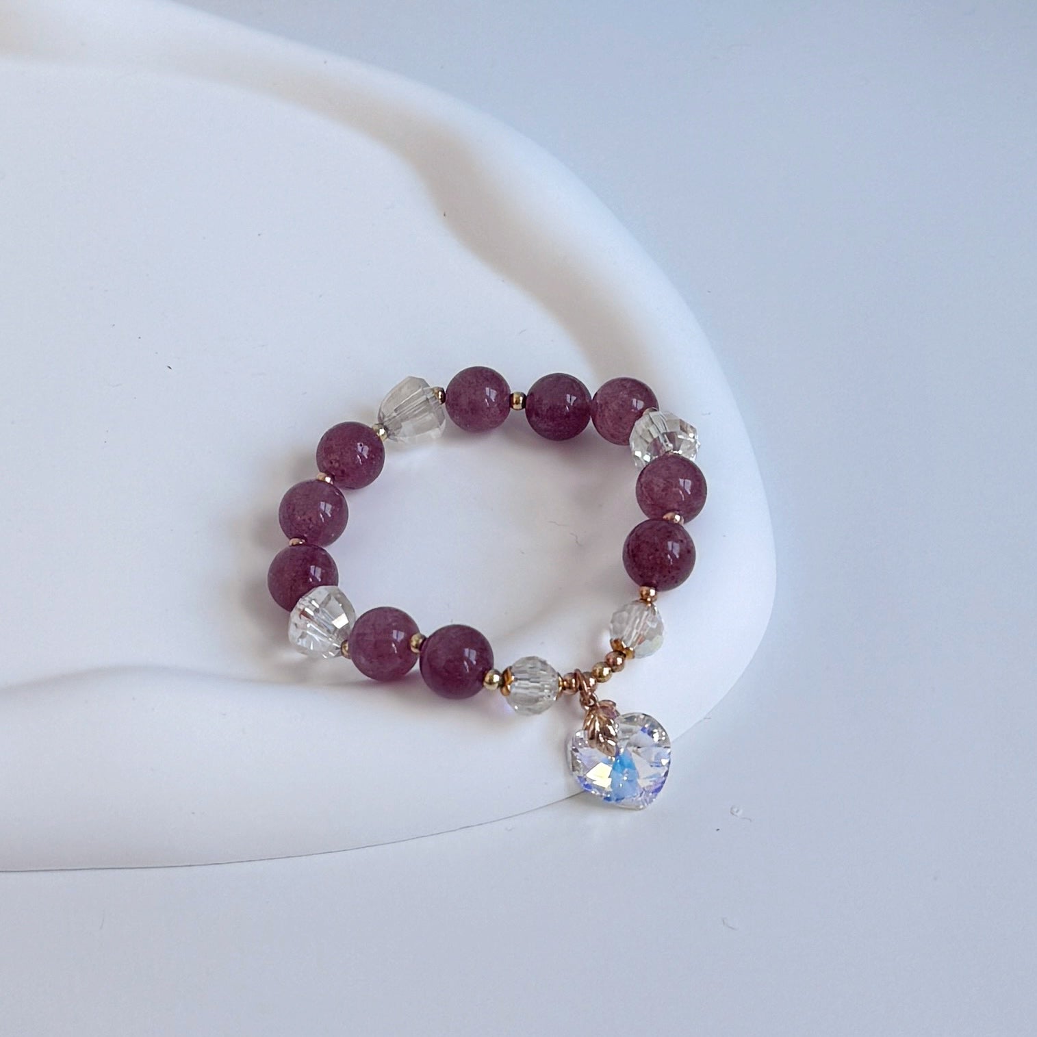 Strawberry quartz bracelet with a darker plum hue, clear glass beads, and a Swarovski heart charm.