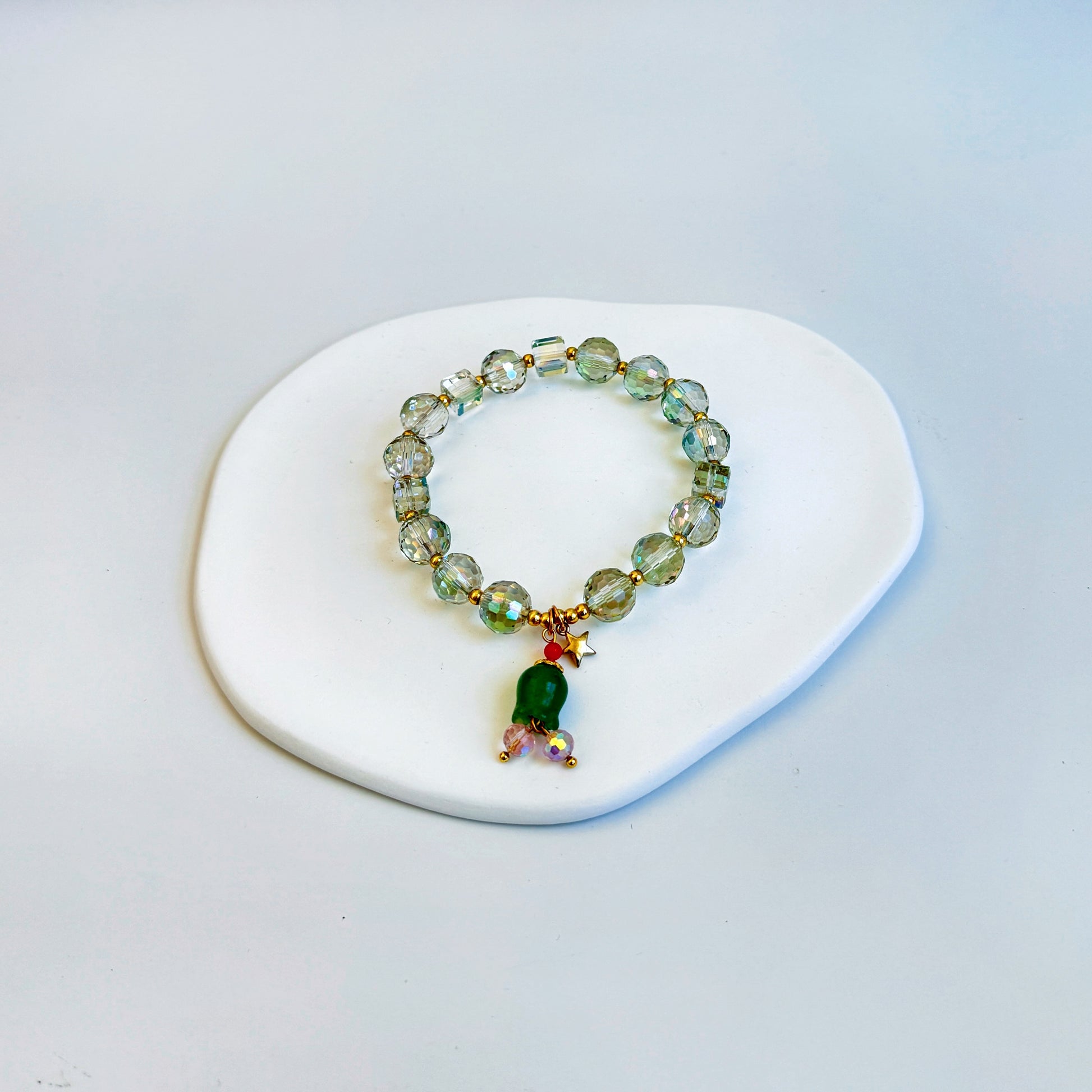 Clear crystal beaded bracelet with a green donglin charm in the shape of a tulip or bluebell flower.