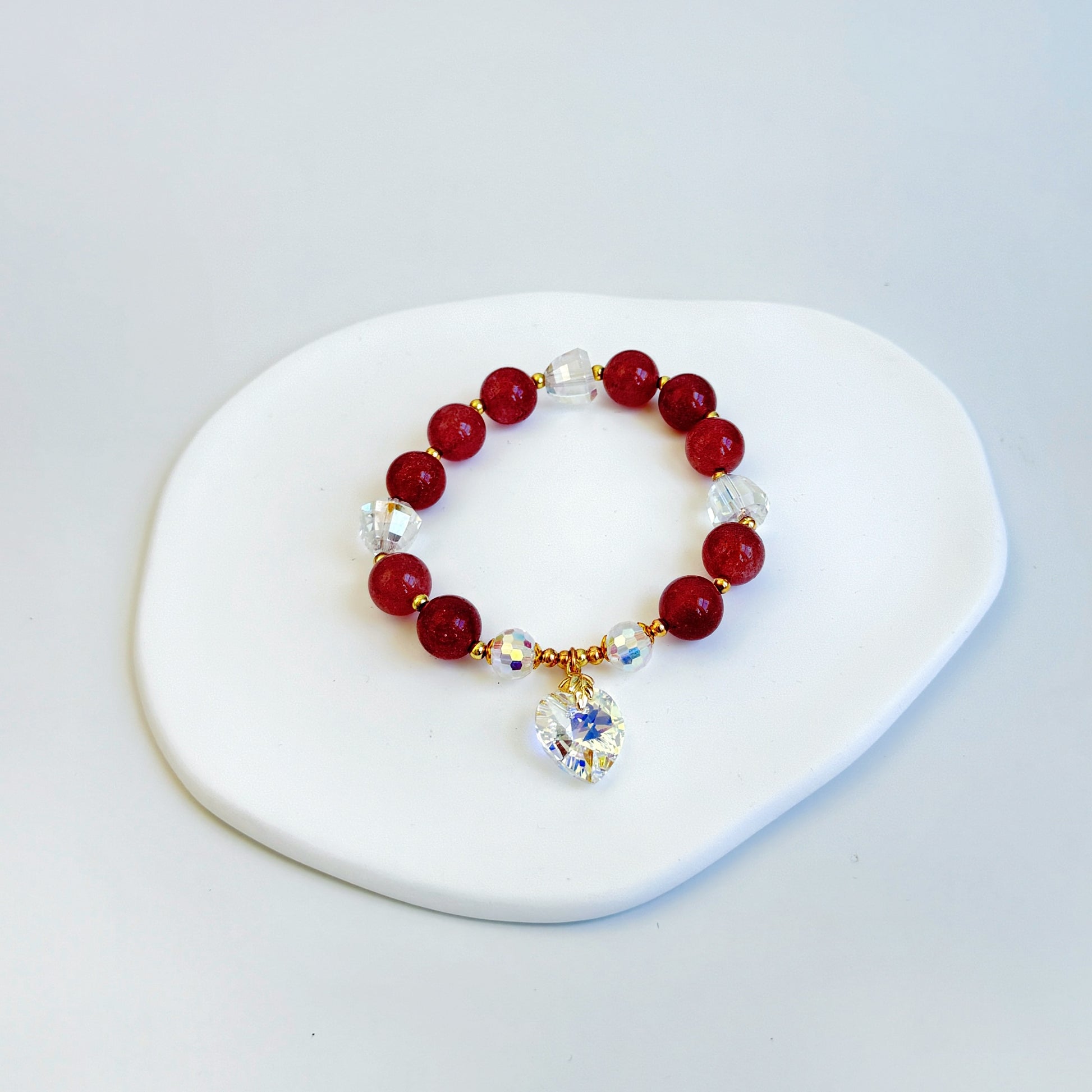 A shimmering and stunning bracelet with plum-hued strawberry quartz beads and a Swarovski heart charm, featuring dark purple/red beads.