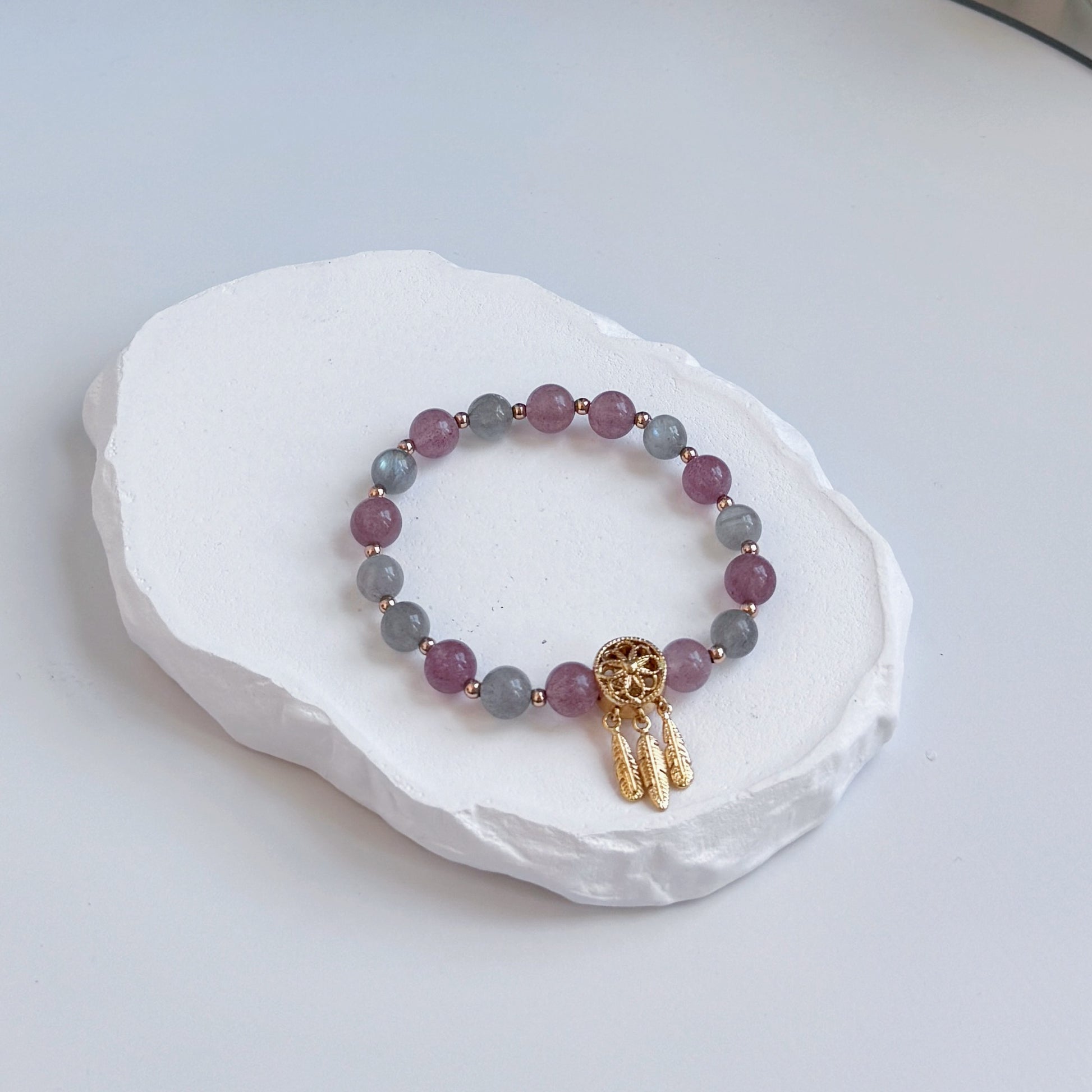 A sophisticated, pretty bracelet with 17 beads alternating between strawberry quartz and moonstone, each separated by a small gold bead, clasped with a gold dreamcatcher bead.