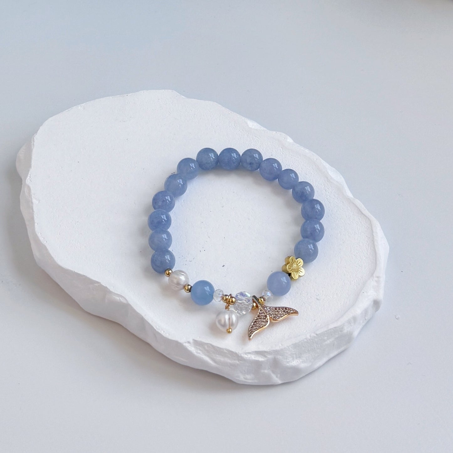 A sophisticated, pretty bracelet with 17 royal blue aquamarine beads with two pearls, a metal flower bead, and a golden colored dolphin tail charm.