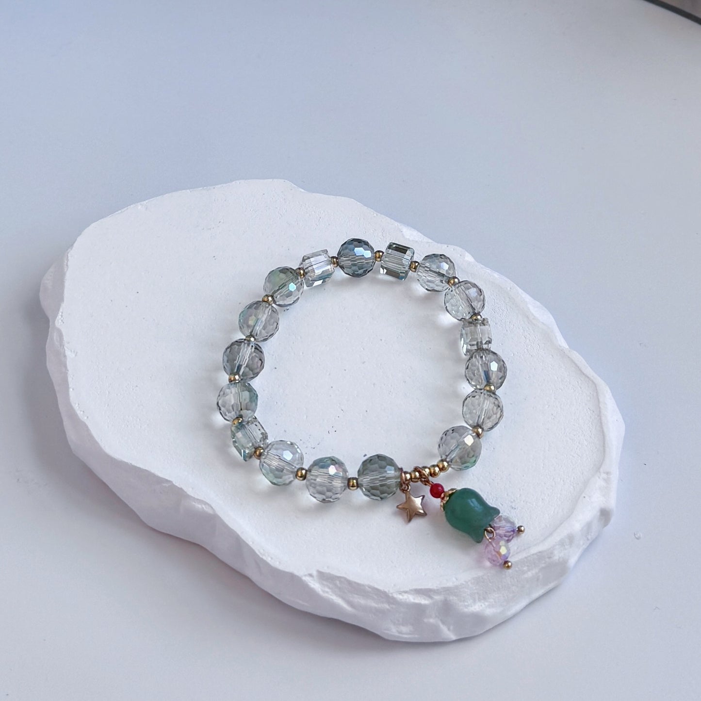 A sophisticated, pretty bracelet with 17 gray crystal beads each separated by a small brass colored metal bead, clasped with a dangling flower charm made of green donglin stone.