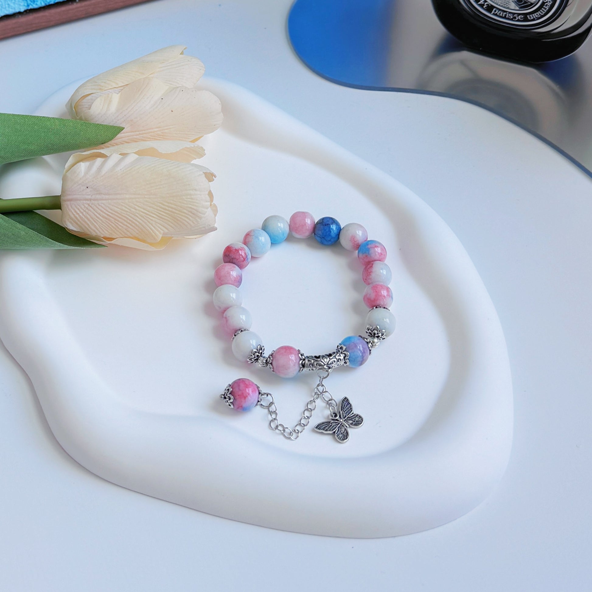 A shining white, blue, and pink bracelet with metal accents, including a butterfly charm.