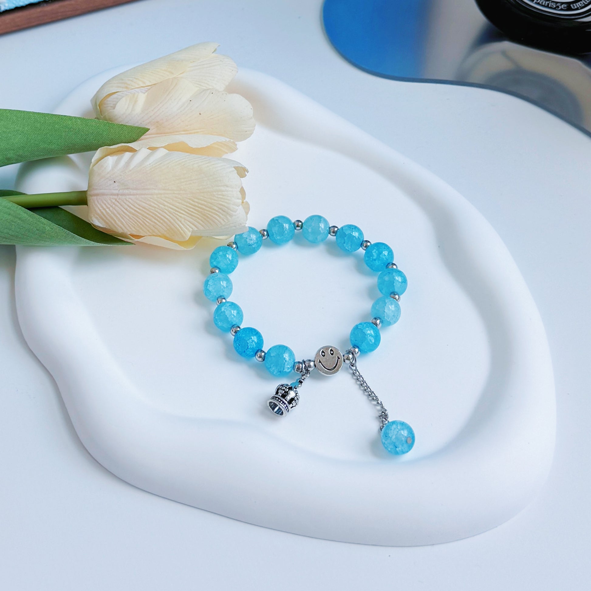 A shining blue bracelet with round glass beads and a metal crown charm.