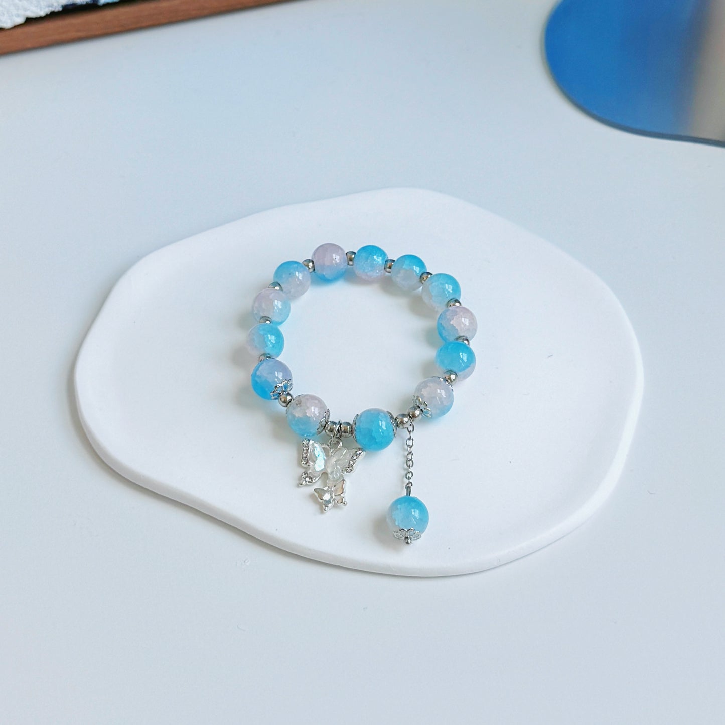 A simple, cute bracelet with light blue and white glass beads and metal accents, including a large and small butterfly charm.