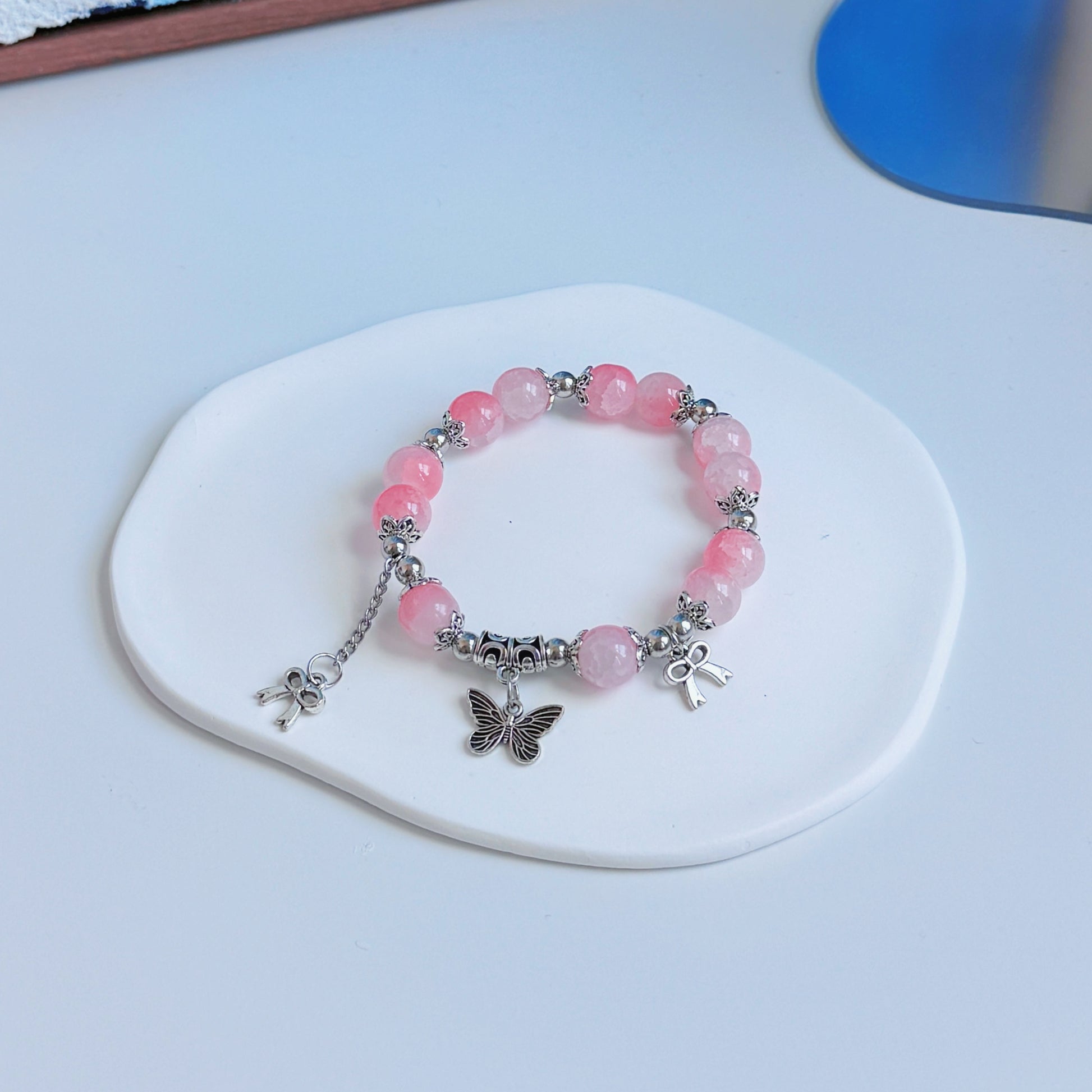 A simple, cute bracelet with light pink glass beads and metal accents, including a butterfly and bow charm, a perfect fashionable accessory for any stylish outfit.