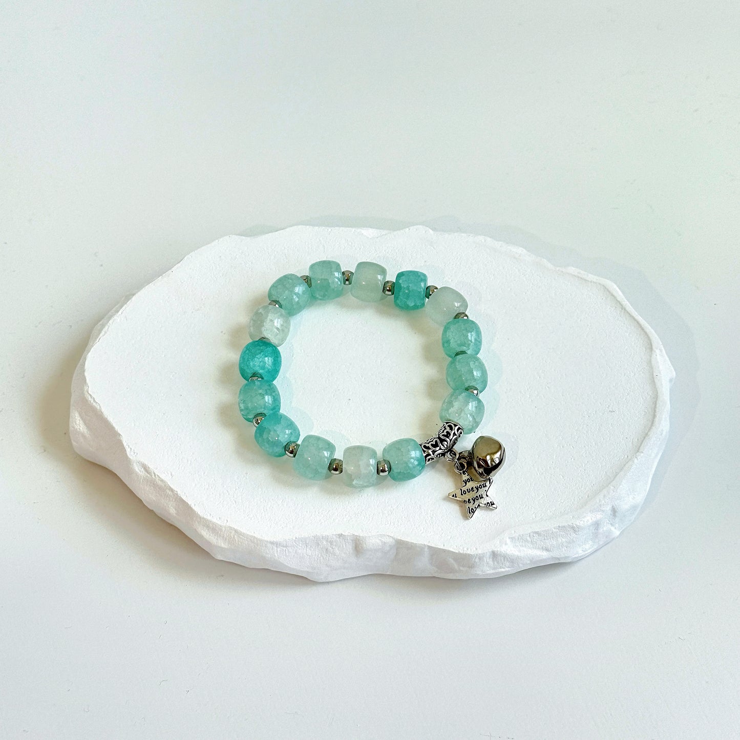 A simple, cute bracelet with 13 light teal glass beads each separated by a small metal bead, clasped with metal bell and star charms.