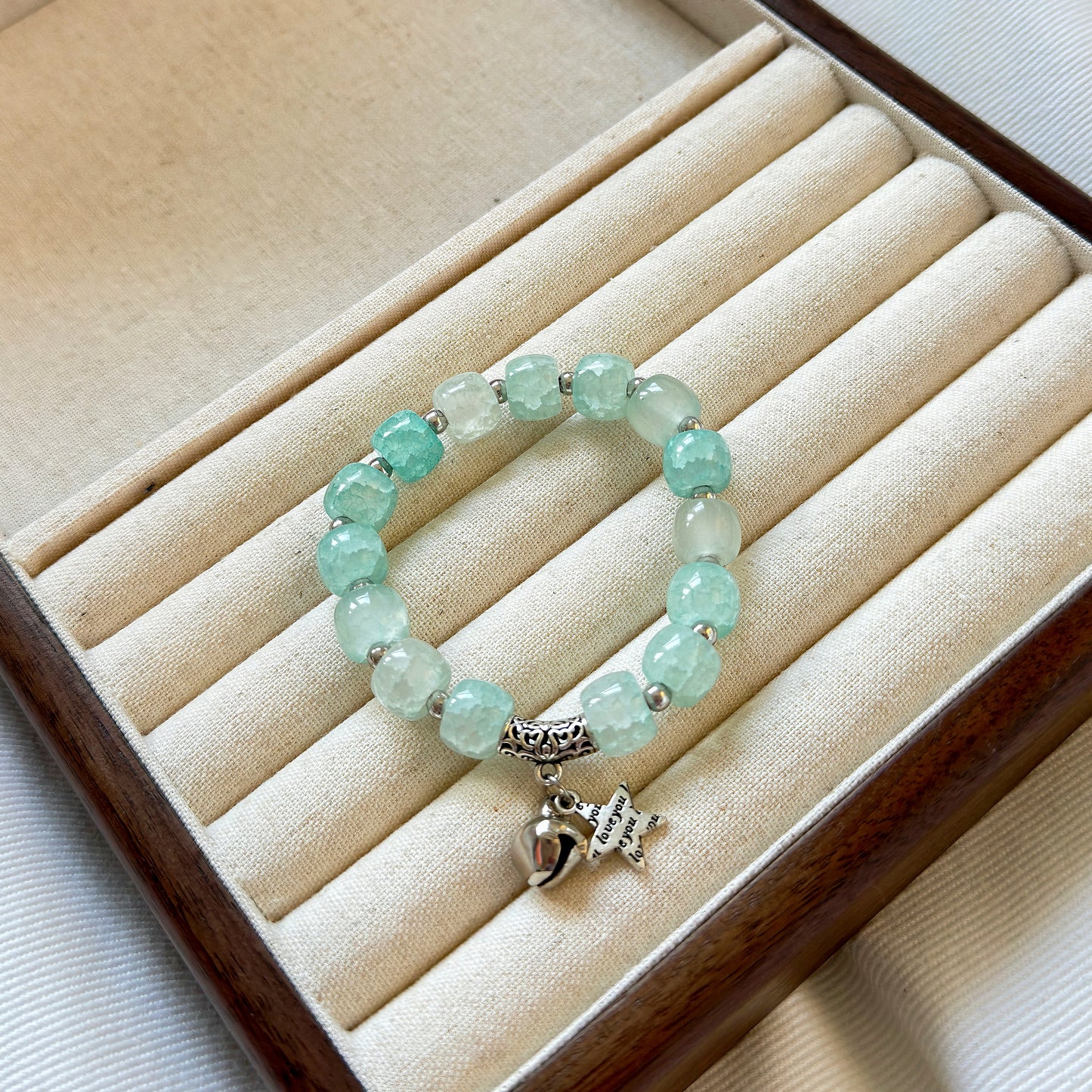 A cute, aqua colored glass bracelet with a bell and star charm, sitting in a warm jewelry tray, ready to be given as a gift for a woman or teen girl, or for a wife, daughter, or girlfriend.