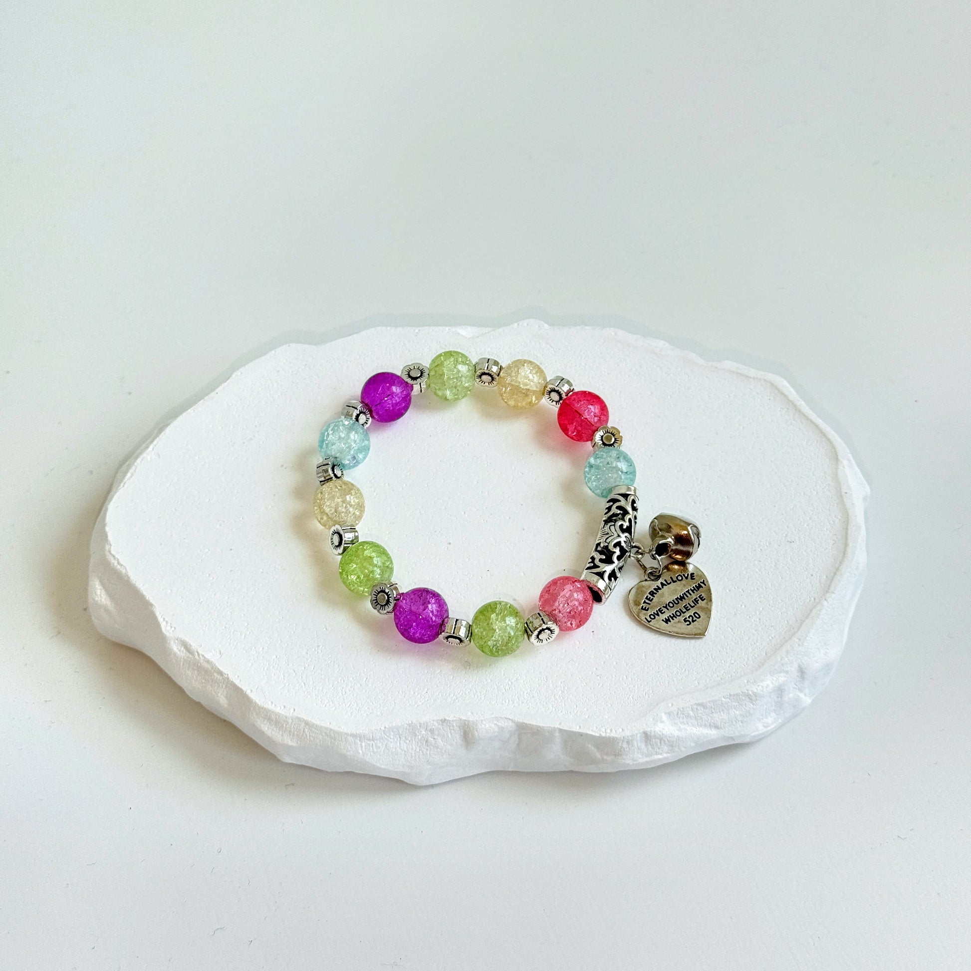 A simple, cute bracelet with 11 glass beads, colored like a wild flower field, each separated by a small metal flower-shaped bead, clasped with metal bell and heart charms.