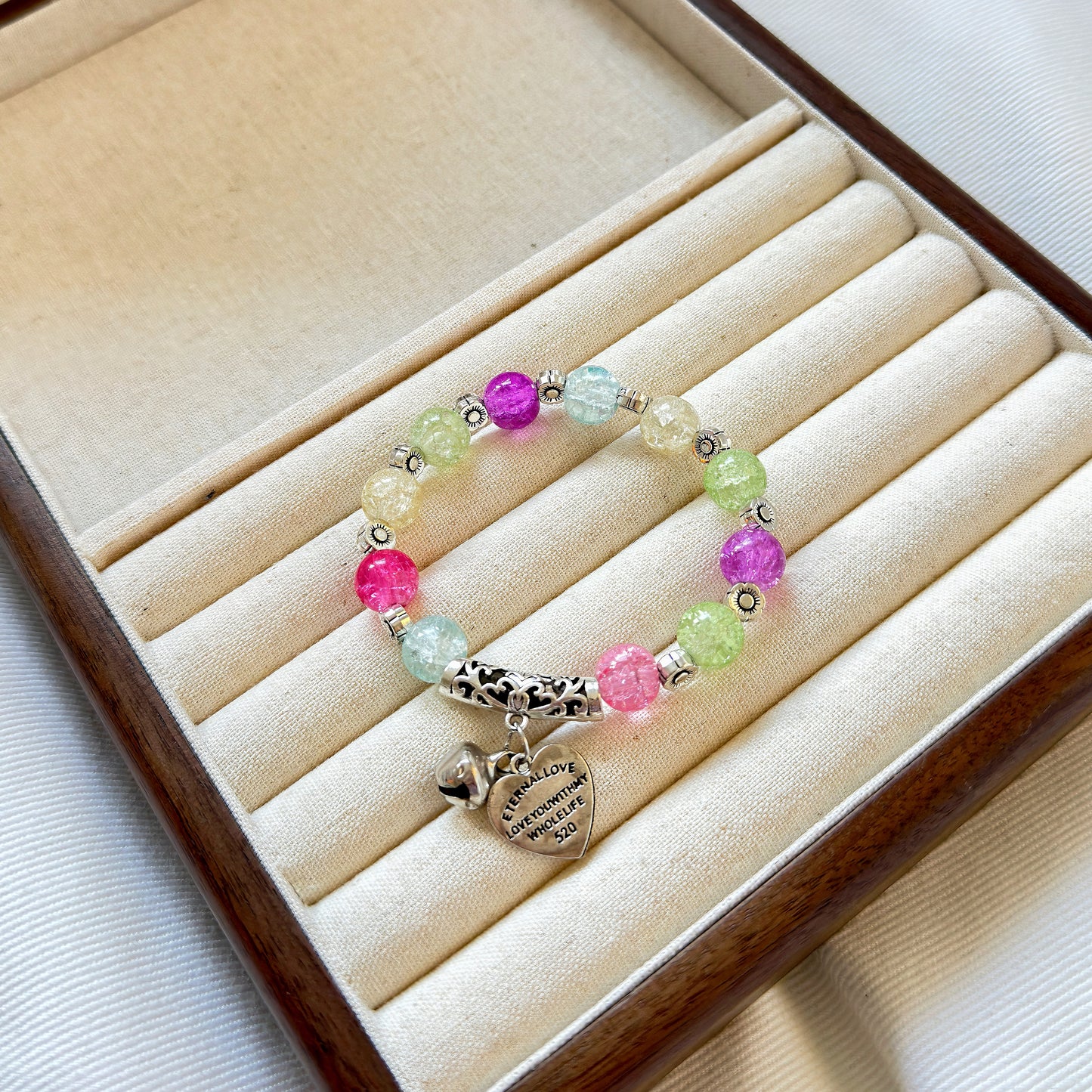 A multicolored bead bracelet, with grassy green, rosy pink, lilac purple, morning glory blue, and tulip white, sitting in a warm jewelry box.