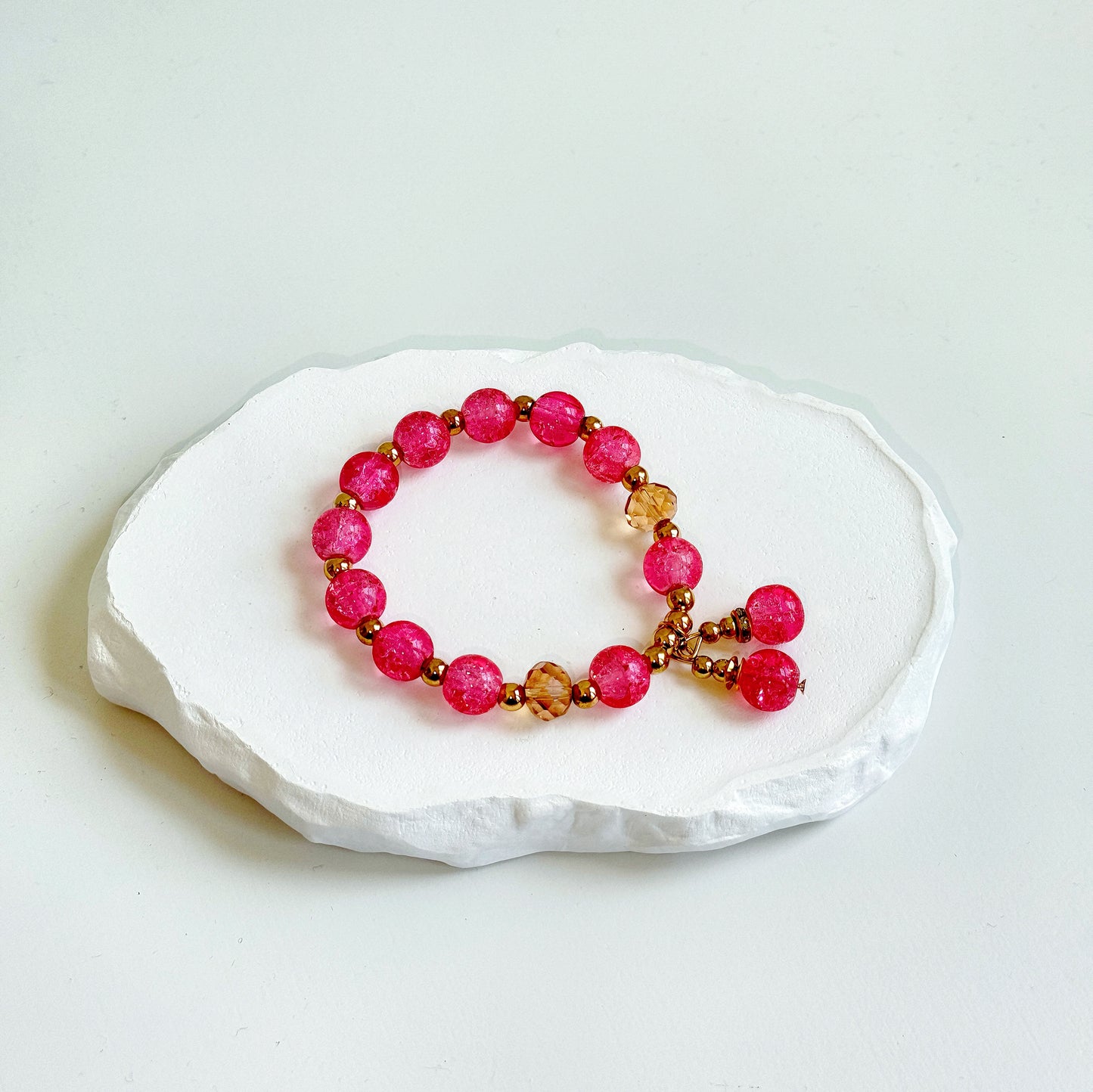 A simple, cute bracelet with 11 hot pink glass beads each separated by a small brass colored metal bead, clasped with a dangling last pair of glass beads.