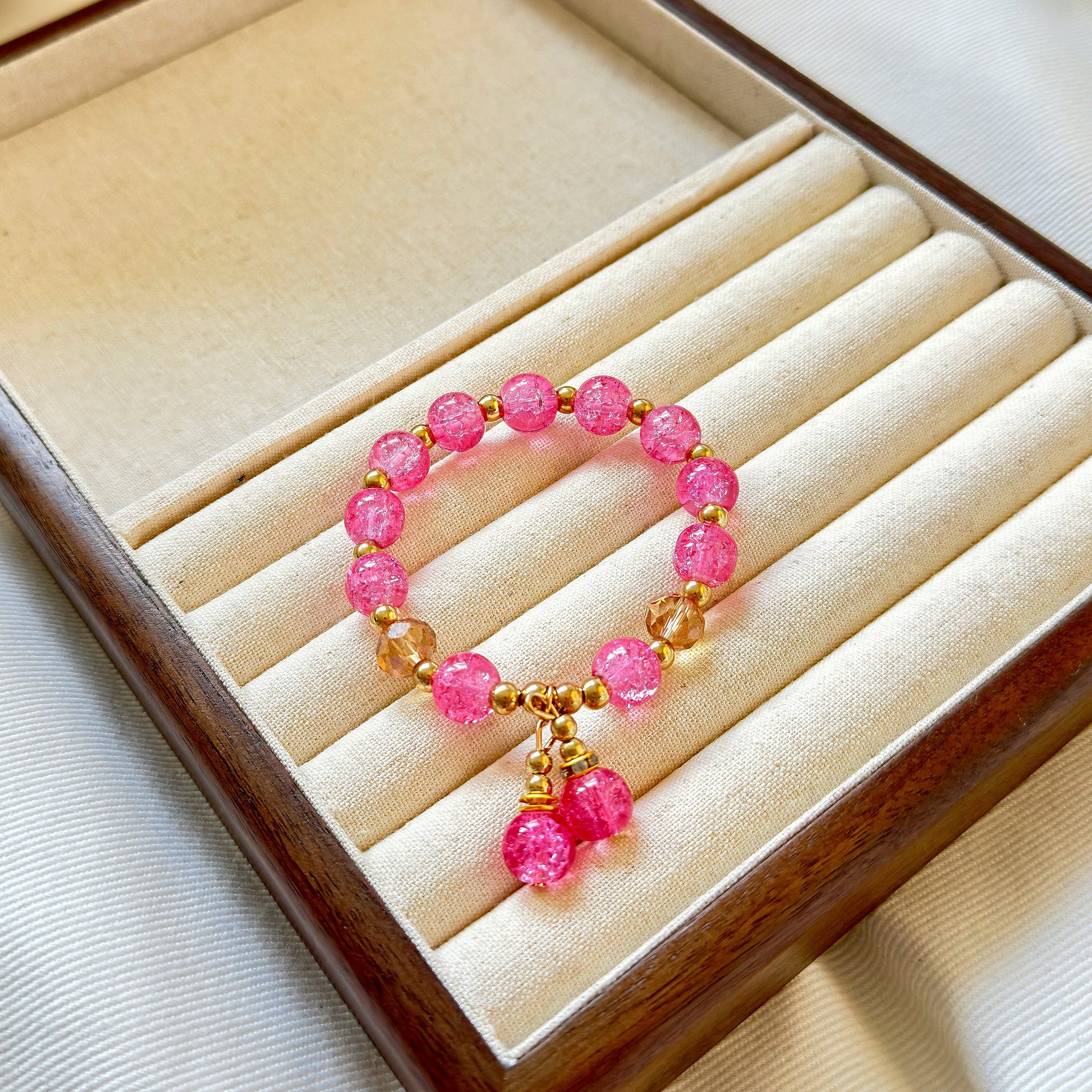 A hot pink glass bead bracelet with bronze accents sitting in a wooden jewelry box, ready to be worn by any teen girl or young woman.