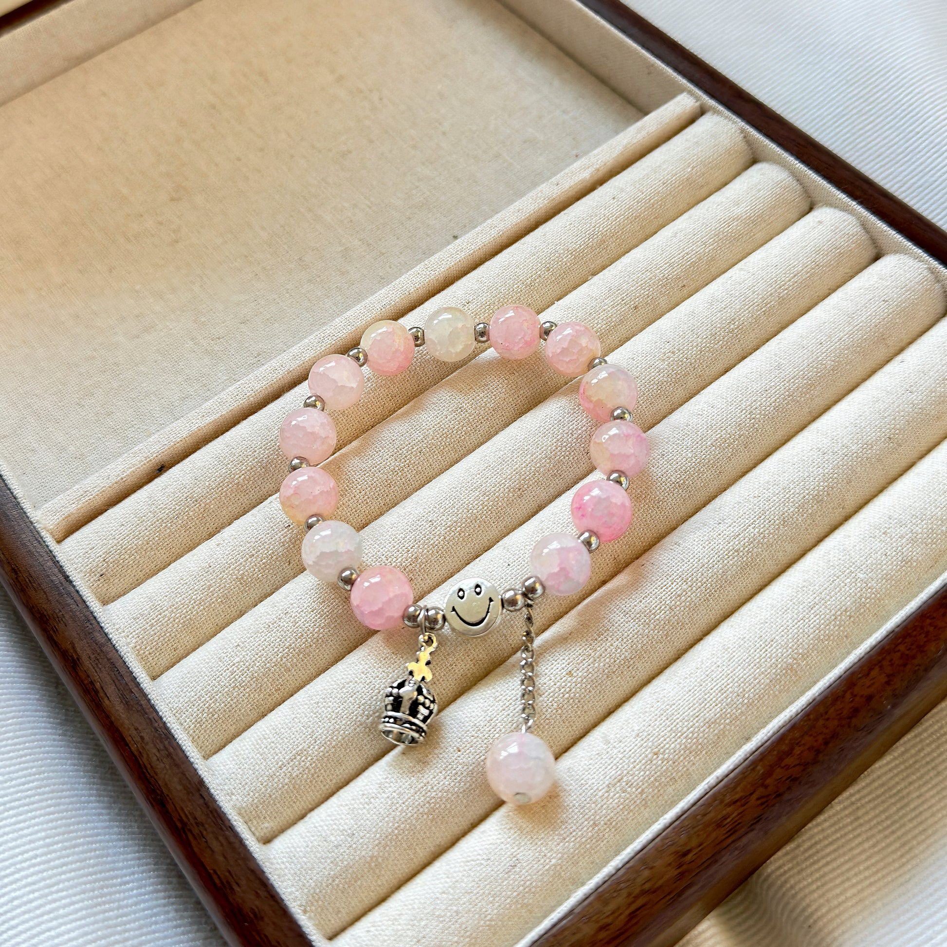 A light pink, cute bracelet with a crown charm made for the queen or princess in your life, sitting in a warm jewelry tray.