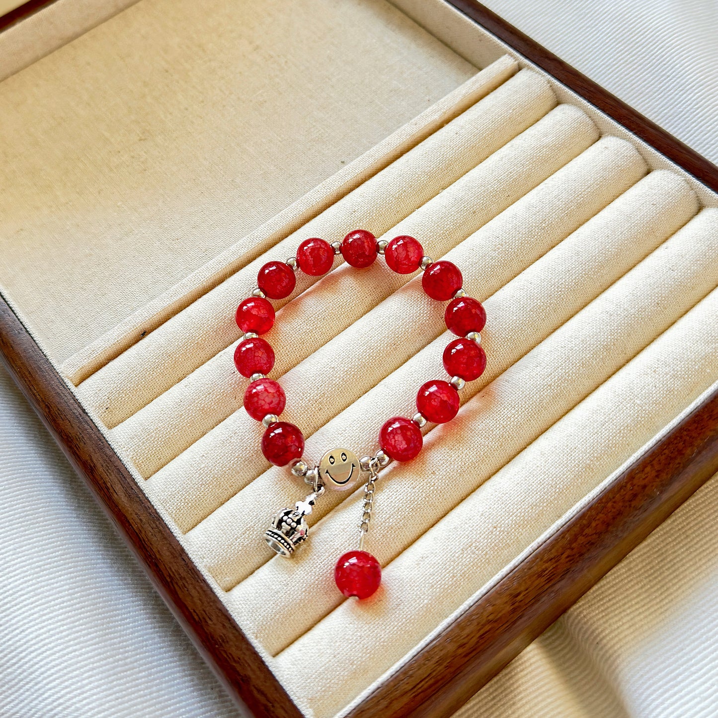 A stunning red glass bead bracelet with a metal crown charm, sitting in a warm jewelry box, ready to be worn by a fashionable young woman or teen girl.