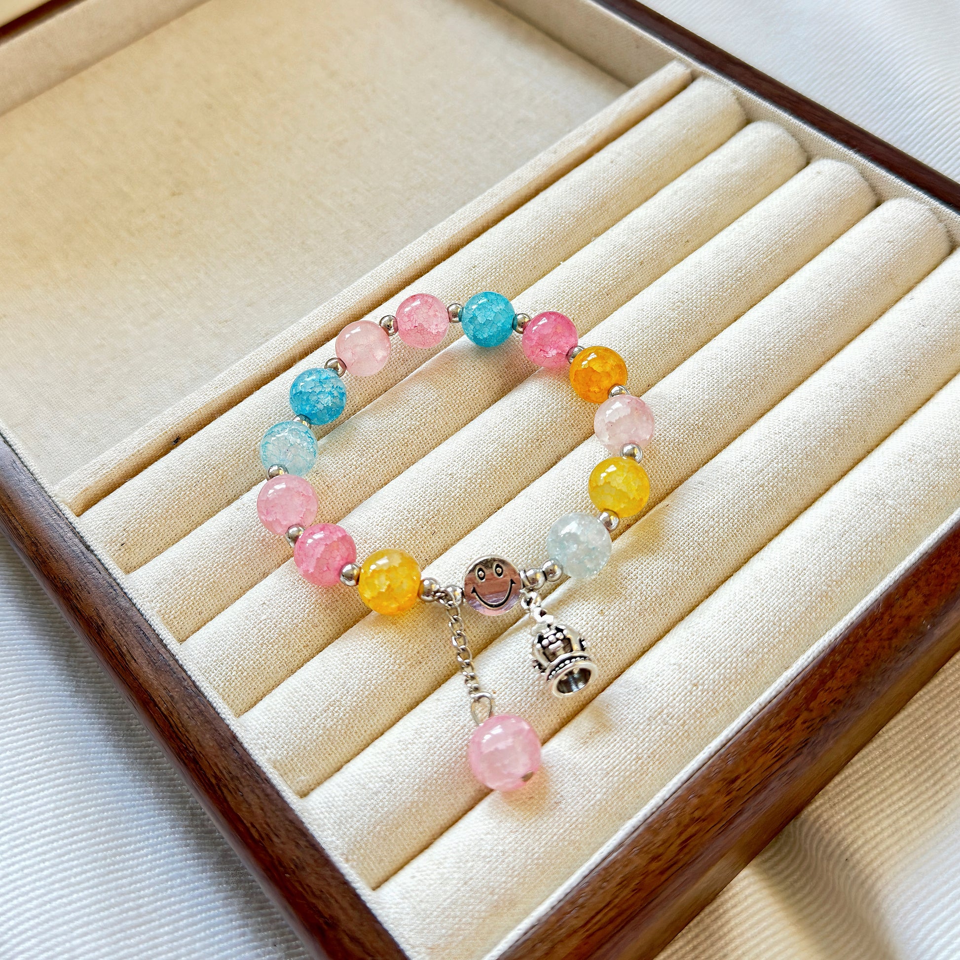 A simple multicolored glass bead bracelet with a crown charm, sitting in a warm jewelry box.