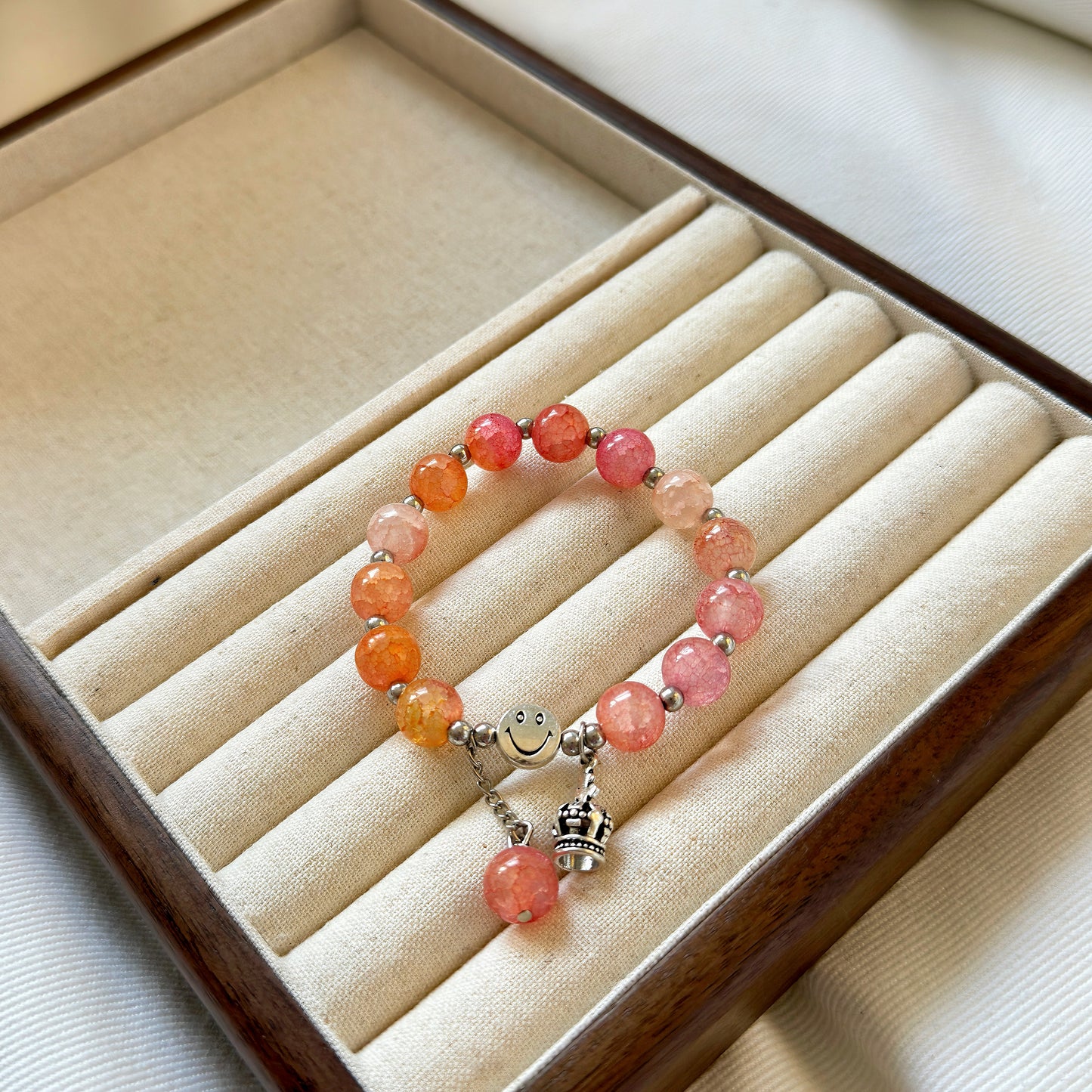 A simple orange and pink glass bracelet, sitting in a warm jewelry box.