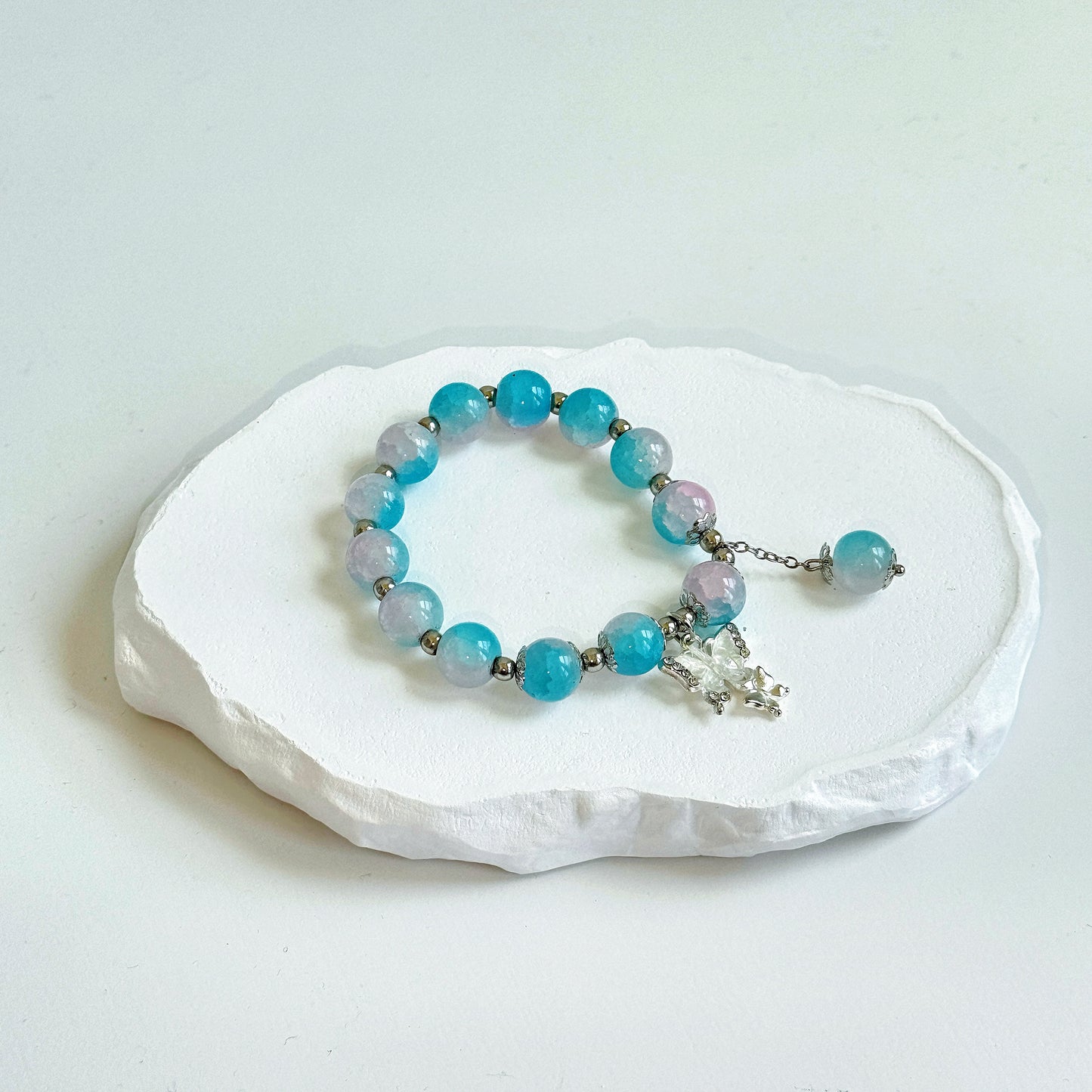 A simple, cute bracelet with 13 crystal white and sky blue glass beads each separated by a small metal bead, tied with a metal butterfly charm and a dangling last glass bead.