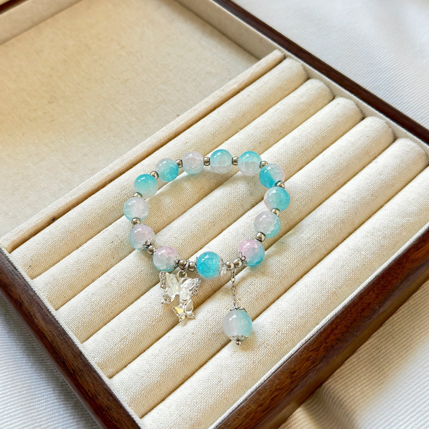 A bright blue bracelet with glass beads appearing as if they are painted with a cloudy sky, sitting in a warm jewelry box.