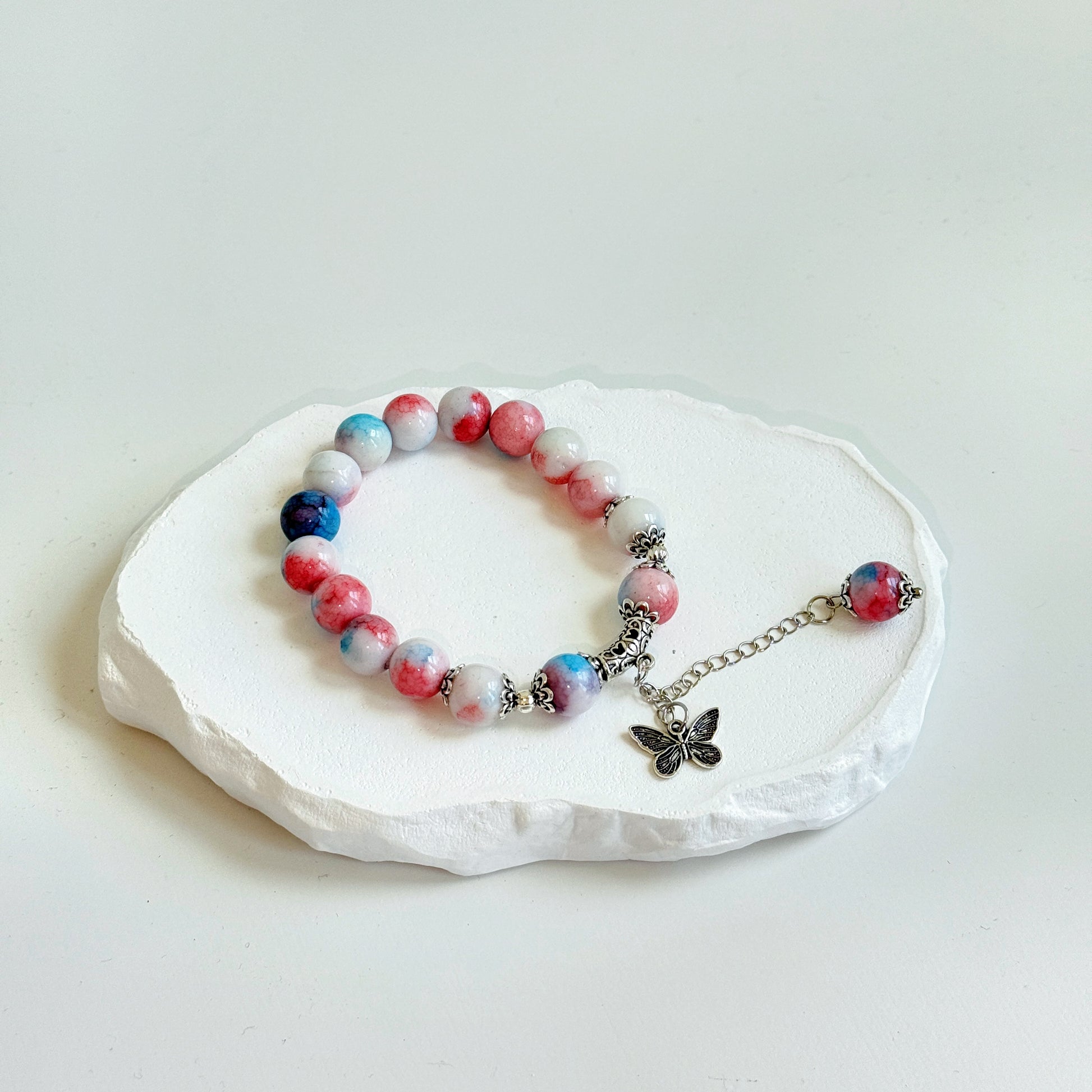 A simple, cute bracelet with 16 opaque white, pink, and blue glass beads, tied with a metal butterfly charm and a dangling last glass bead, with metal accents adorning the piece.